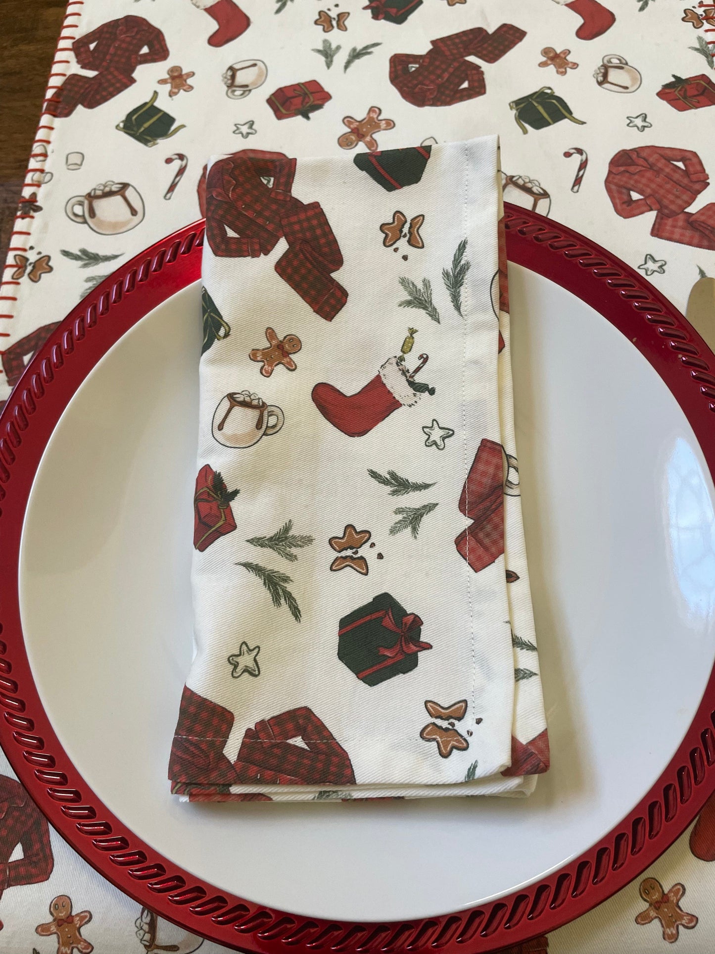 A folded white cotton napkin with a red plaid pattern and Christmas-themed decorations such as snowflakes, bears, and pinecones, placed on a circular red plate with a Christmas-themed pattern.