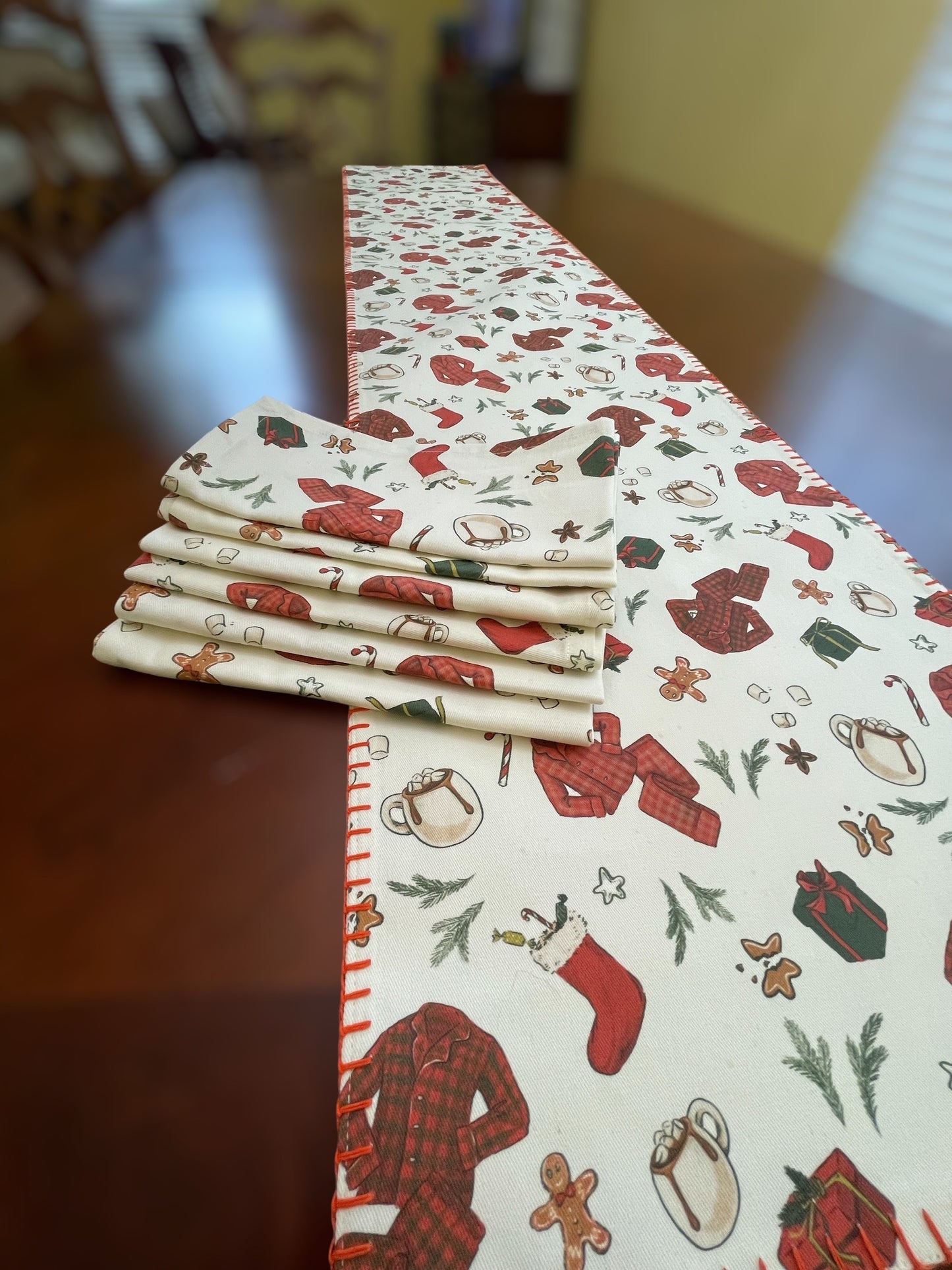 Stack of folded napkins next to a Christmas-themed table runner on a wooden table.