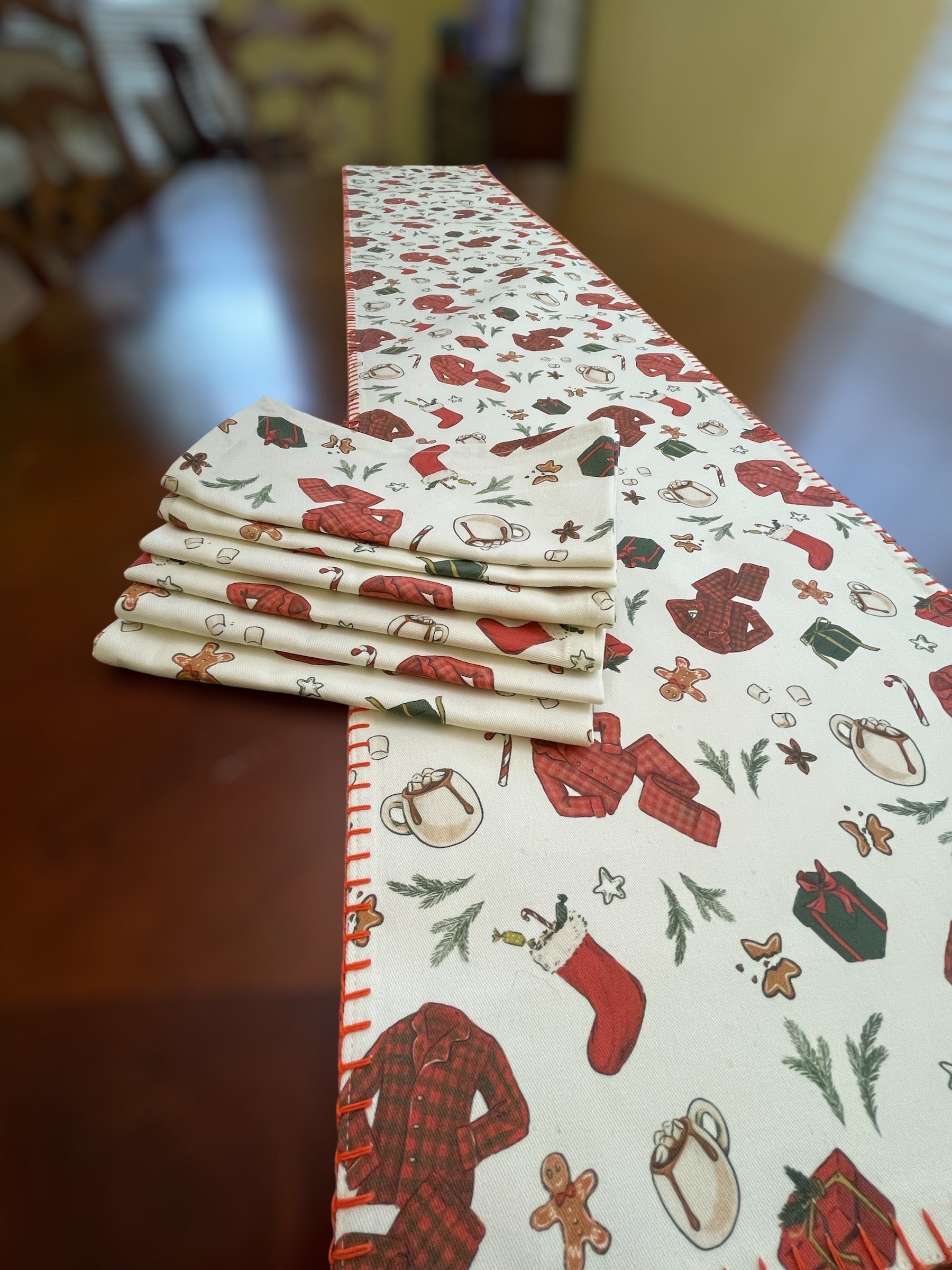 Stack of folded napkins next to a Christmas-themed table runner on a wooden table.