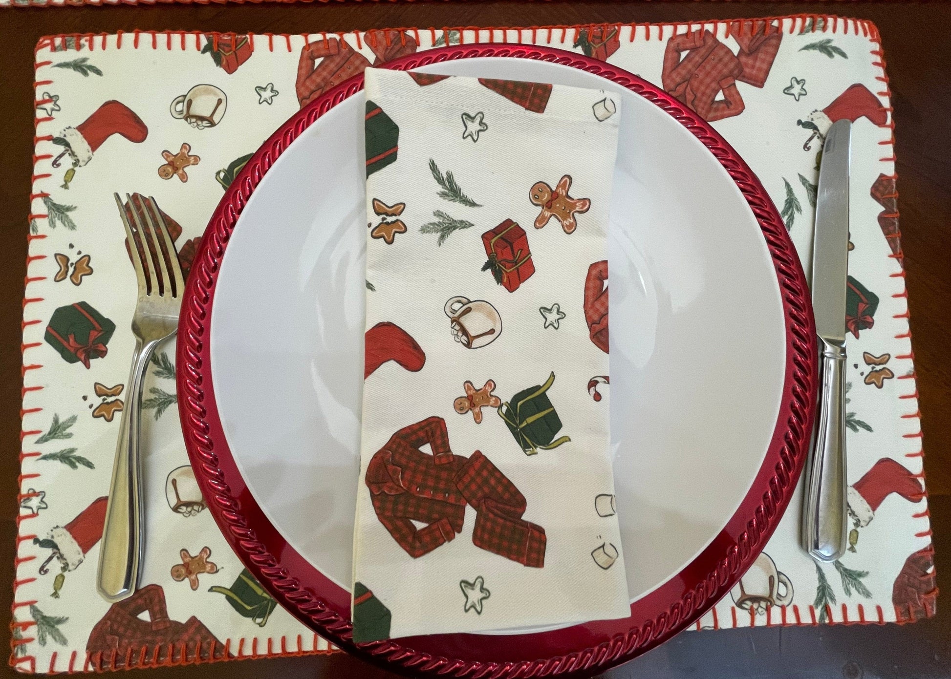 Anghild's Table Placemat Christmas Morning Placemats set of 2 Christmas Morning Placemats set of 2 Anghild's Table Christmas Morning Cotton placemat with chritmas morning motif of buffalo check PJs, candy canes, Christmas  stockings, wrapped gifts and Christmas cookies on an off white background and red whip sticking trim.
Christmas Morning cotton napkin on plate.